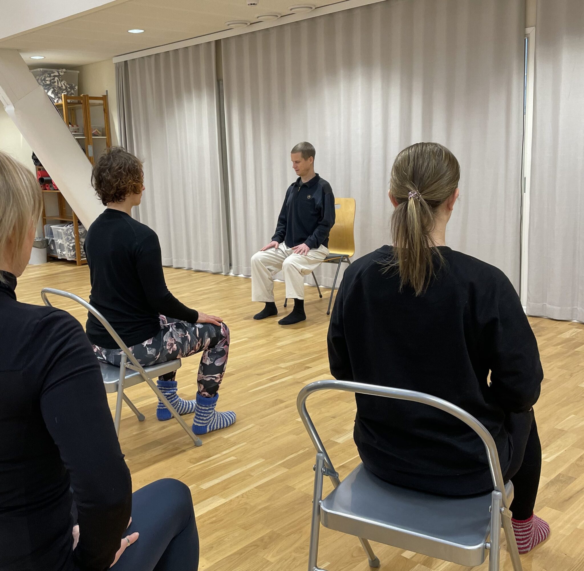 Meditaatiohetki salissa. Kouluttaja Janne Kontala istuu ryhdikkäästi tuolilla. Oppilaat istuvat tuoleilla.